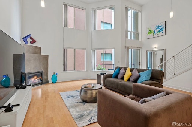 living area featuring a glass covered fireplace, stairway, wood finished floors, and a towering ceiling