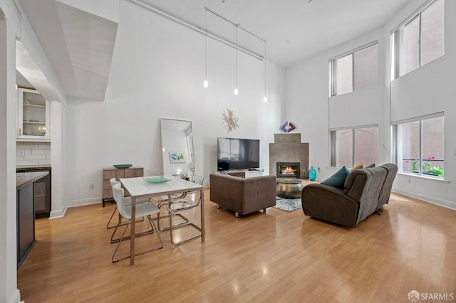 living area featuring a high ceiling, a lit fireplace, a wealth of natural light, and light wood-type flooring