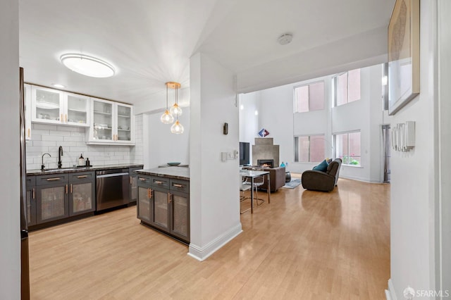 kitchen featuring stainless steel dishwasher, backsplash, baseboards, and light wood finished floors