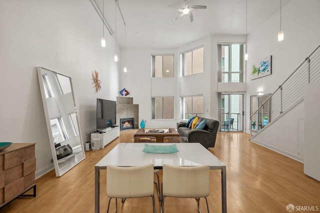 dining space with a high ceiling, a glass covered fireplace, ceiling fan, and light wood-type flooring