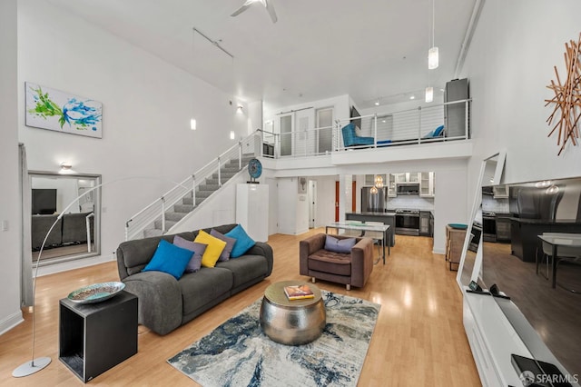 living room with light wood-type flooring, a ceiling fan, stairs, and a high ceiling
