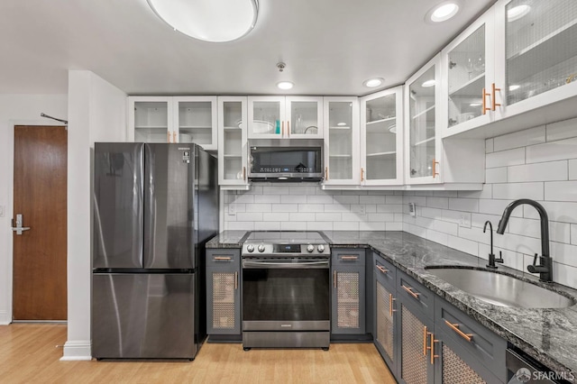 kitchen with white cabinets, a sink, light wood finished floors, dark stone counters, and stainless steel appliances