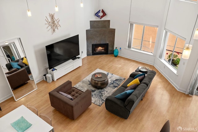 living room featuring baseboards, a lit fireplace, wood finished floors, and a towering ceiling