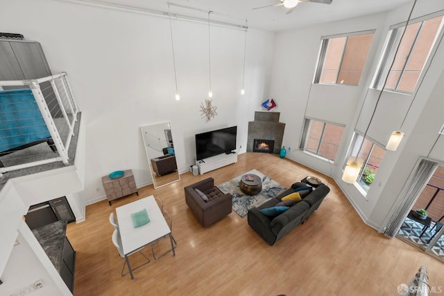 living area featuring wood finished floors, ceiling fan, a high ceiling, and a lit fireplace