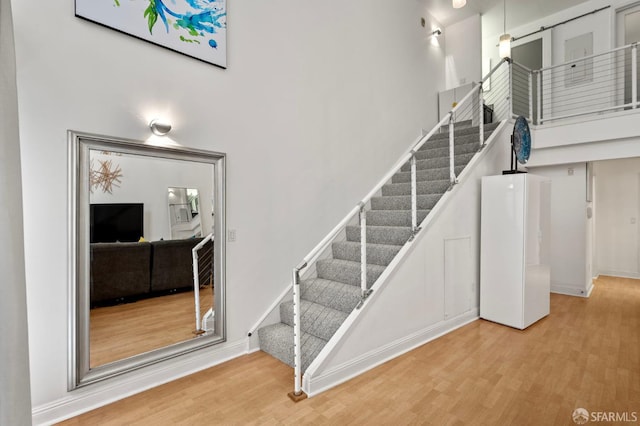 stairs with baseboards, a high ceiling, and wood finished floors