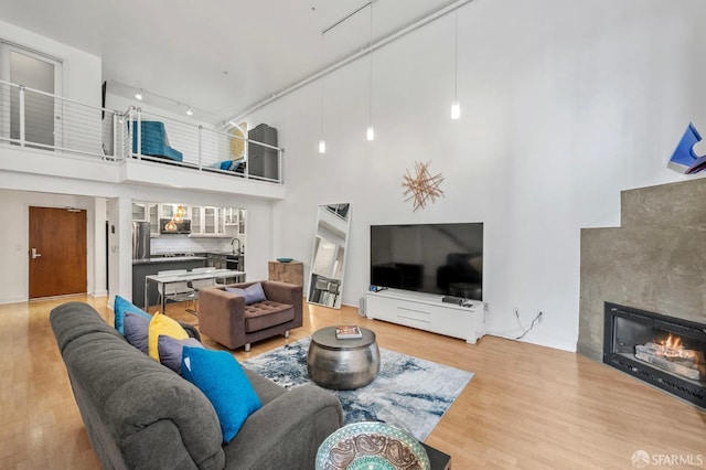living room featuring track lighting, a premium fireplace, light wood finished floors, and a towering ceiling
