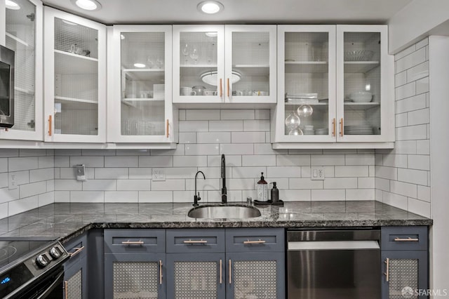 kitchen with a sink, dishwasher, dark stone counters, decorative backsplash, and glass insert cabinets