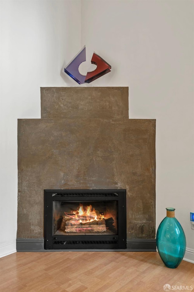 interior details featuring baseboards, a warm lit fireplace, and wood finished floors