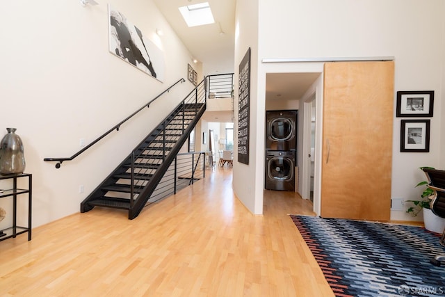 entryway featuring hardwood / wood-style floors, a skylight, stacked washer and clothes dryer, and a high ceiling