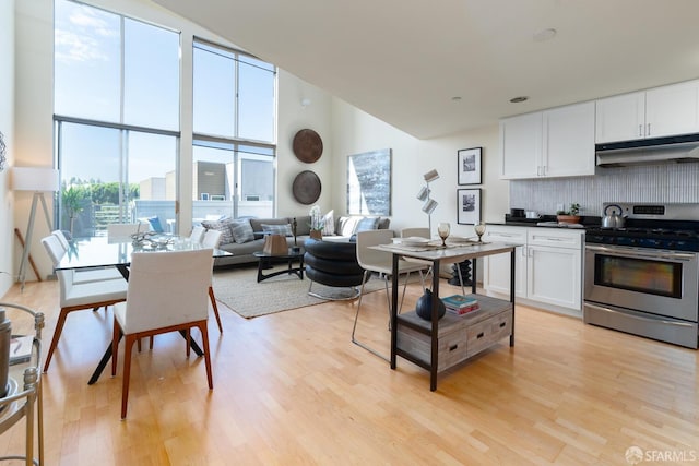 kitchen with white cabinetry, decorative backsplash, a high ceiling, stainless steel range oven, and light wood-type flooring