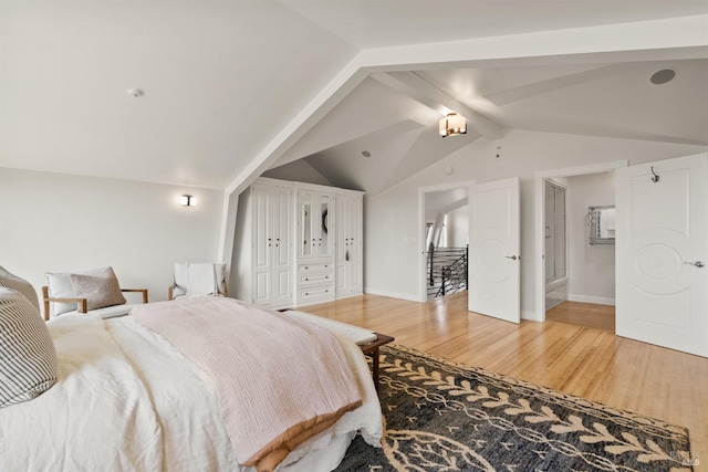 bedroom featuring baseboards, light wood-style flooring, and vaulted ceiling with beams