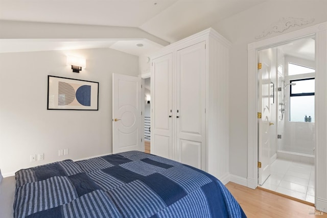 bedroom with baseboards, vaulted ceiling, light wood finished floors, and ensuite bath