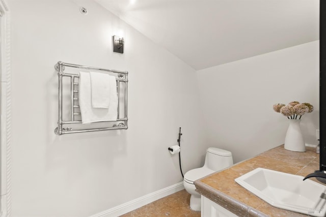 bathroom featuring baseboards, vaulted ceiling, toilet, and vanity