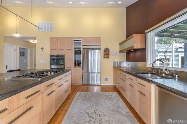 kitchen featuring light brown cabinetry, light wood-type flooring, stainless steel appliances, sink, and decorative light fixtures