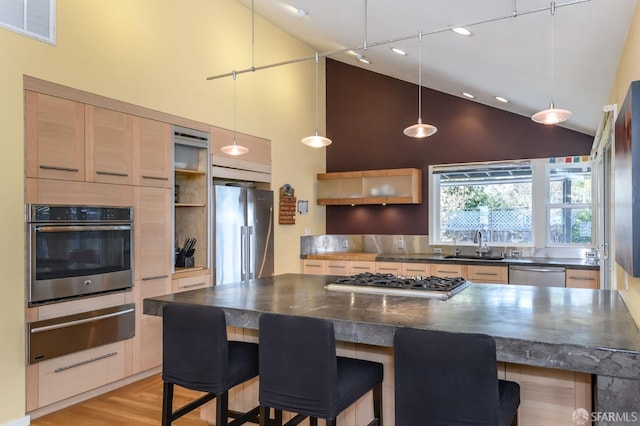 kitchen with appliances with stainless steel finishes, a kitchen island, light hardwood / wood-style floors, high vaulted ceiling, and a breakfast bar