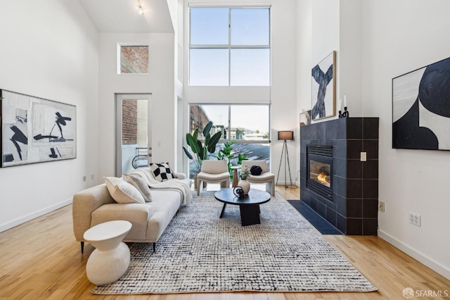 living room featuring hardwood / wood-style flooring, a towering ceiling, and a tiled fireplace