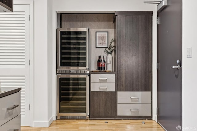 bar featuring beverage cooler, dark brown cabinets, and light wood-type flooring