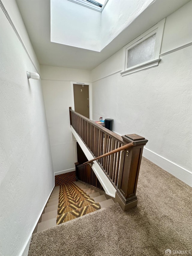 stairway with a textured wall, carpet floors, a skylight, and baseboards