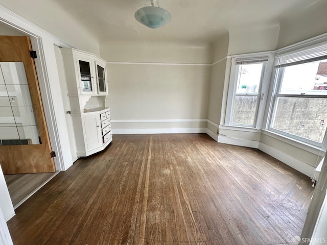 unfurnished dining area featuring baseboards and dark wood-type flooring