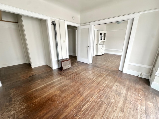 unfurnished bedroom featuring heating unit, two closets, and hardwood / wood-style floors