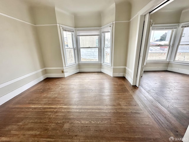 unfurnished room with dark wood-style floors, a wealth of natural light, and baseboards