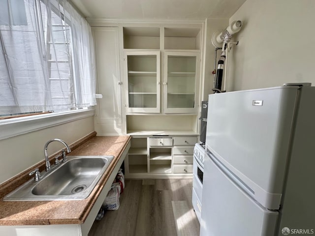 kitchen with dark wood-type flooring, a sink, white cabinets, freestanding refrigerator, and glass insert cabinets