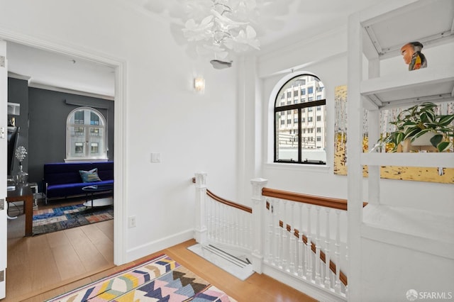 staircase with an inviting chandelier, ornamental molding, baseboards, and wood finished floors