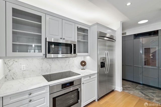 kitchen with stainless steel appliances, light stone counters, decorative backsplash, glass insert cabinets, and light wood-style floors