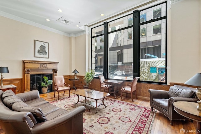 interior space with wood finished floors, a wainscoted wall, visible vents, ornamental molding, and a high end fireplace