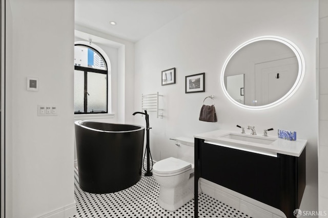 bathroom featuring toilet, baseboards, a soaking tub, and vanity
