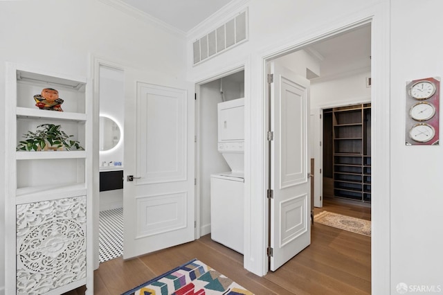 washroom featuring stacked washer and clothes dryer, dark wood finished floors, visible vents, and ornamental molding