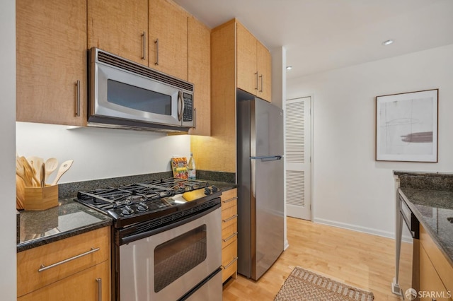 kitchen with dark stone counters, stainless steel appliances, and light hardwood / wood-style floors