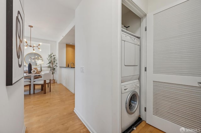 washroom featuring a chandelier, light wood-type flooring, and stacked washing maching and dryer