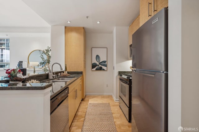 kitchen with sink, stainless steel appliances, kitchen peninsula, dark stone counters, and light wood-type flooring