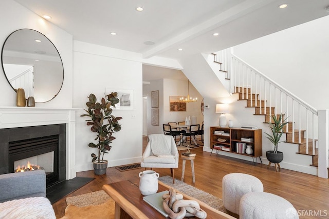 living area with wood finished floors, stairway, a glass covered fireplace, and beam ceiling