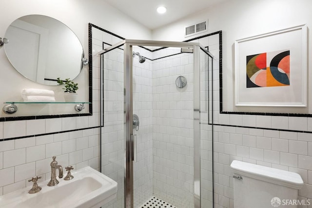 bathroom featuring toilet, a sink, visible vents, tile walls, and a shower stall