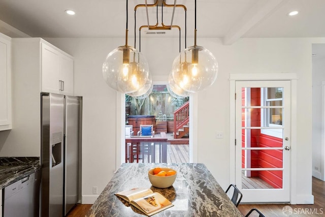 kitchen featuring appliances with stainless steel finishes, white cabinetry, wood finished floors, dark stone counters, and beamed ceiling