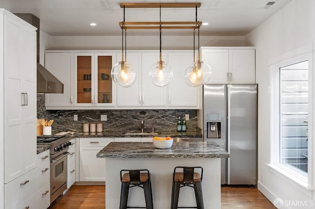 kitchen with a sink, visible vents, wall chimney range hood, appliances with stainless steel finishes, and decorative backsplash