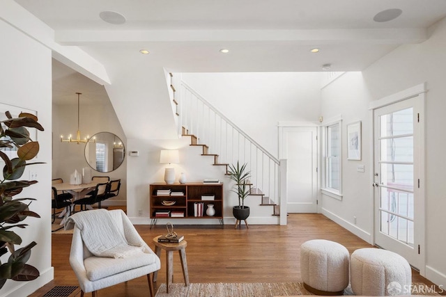 entrance foyer with beam ceiling, a notable chandelier, wood finished floors, baseboards, and stairs