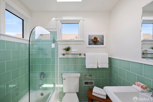 bathroom featuring shower / bathing tub combination, plenty of natural light, toilet, and tile walls