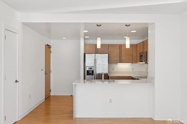 kitchen featuring kitchen peninsula, appliances with stainless steel finishes, sink, decorative light fixtures, and light hardwood / wood-style flooring