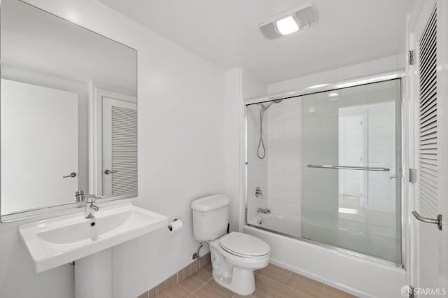 bathroom with tile patterned floors, bath / shower combo with glass door, and toilet