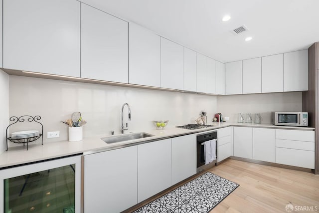 kitchen featuring visible vents, black oven, wine cooler, stainless steel microwave, and a sink