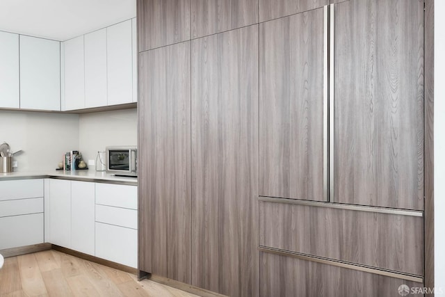 kitchen with modern cabinets, light wood-type flooring, light countertops, stainless steel microwave, and white cabinetry