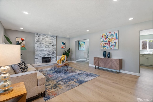 living room with a textured ceiling, sink, a fireplace, and light hardwood / wood-style flooring