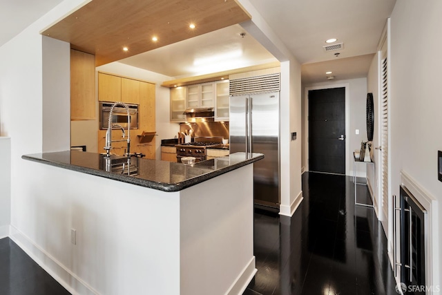 kitchen with high end appliances, baseboards, a peninsula, a sink, and recessed lighting