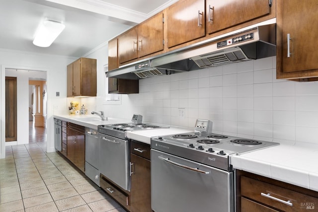 kitchen with tile counters, stainless steel appliances, crown molding, backsplash, and sink