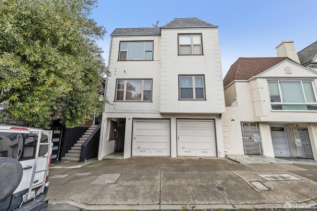 townhome / multi-family property featuring a garage, driveway, stairs, and stucco siding