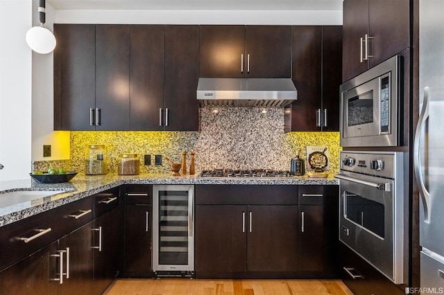 kitchen featuring appliances with stainless steel finishes, beverage cooler, range hood, light stone counters, and light hardwood / wood-style flooring