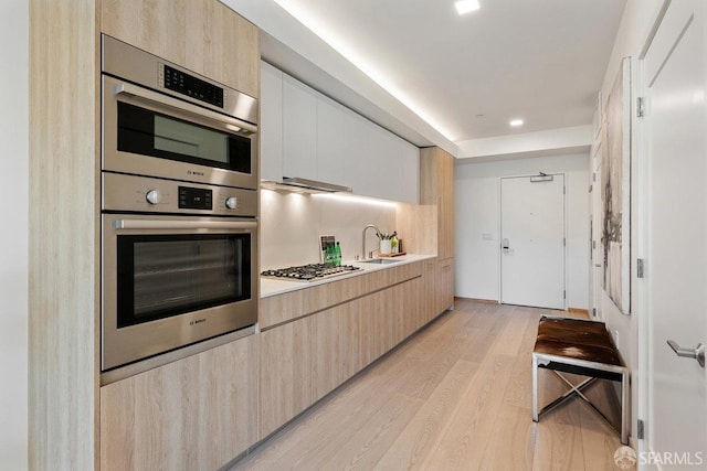 kitchen featuring light wood-type flooring, stainless steel appliances, sink, backsplash, and light brown cabinetry